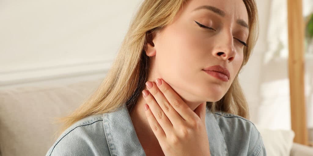Kobieta trzymająca się za szyję i mrużąca oczy, cierpiąca na zapalenie przełyku