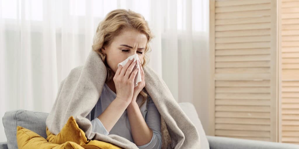 Kobieta z objawami choroby na kanapie wydmuchuje nos w chusteczkę po tym, jak wykonała testy na RSV